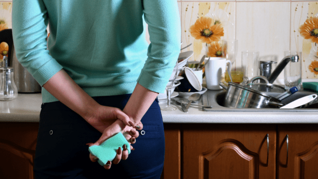 Person facing a sink of dirty dishes with a sponge in hand