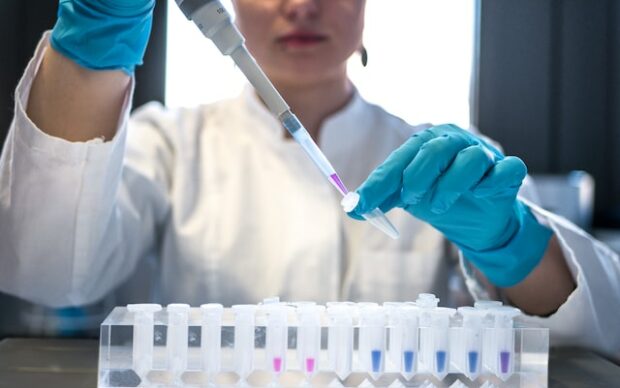 Female scientist pipetting coloured chemicals into a tube.