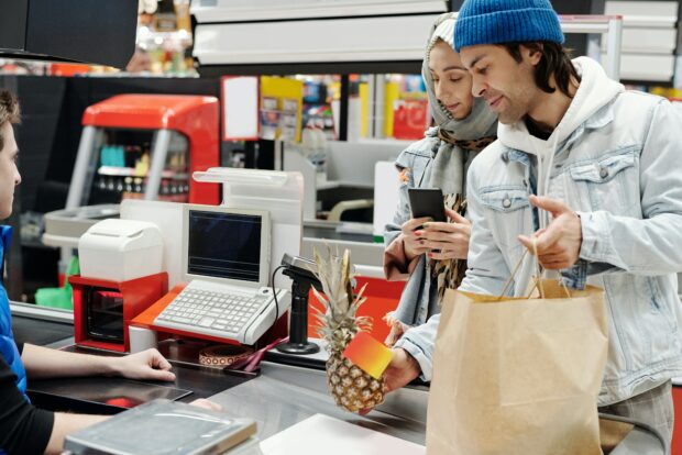 A couple at a supermarket checkout handing over a pineapple