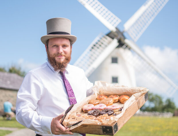 Richard from Melin Llynon holding a box of pastries in front of a windmill