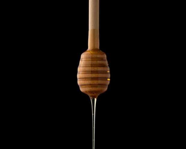 Wooden dipper with honey on dripping downwards